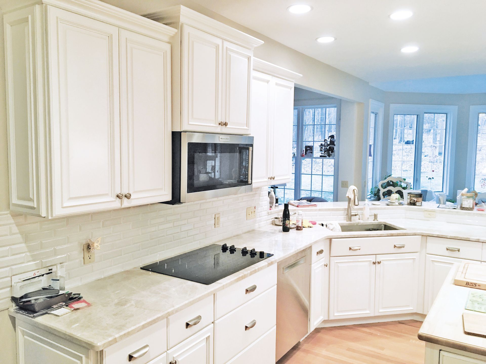 A bright kitchen with white cabinets, a glass cooktop, stainless steel dishwasher, and beige countertops.