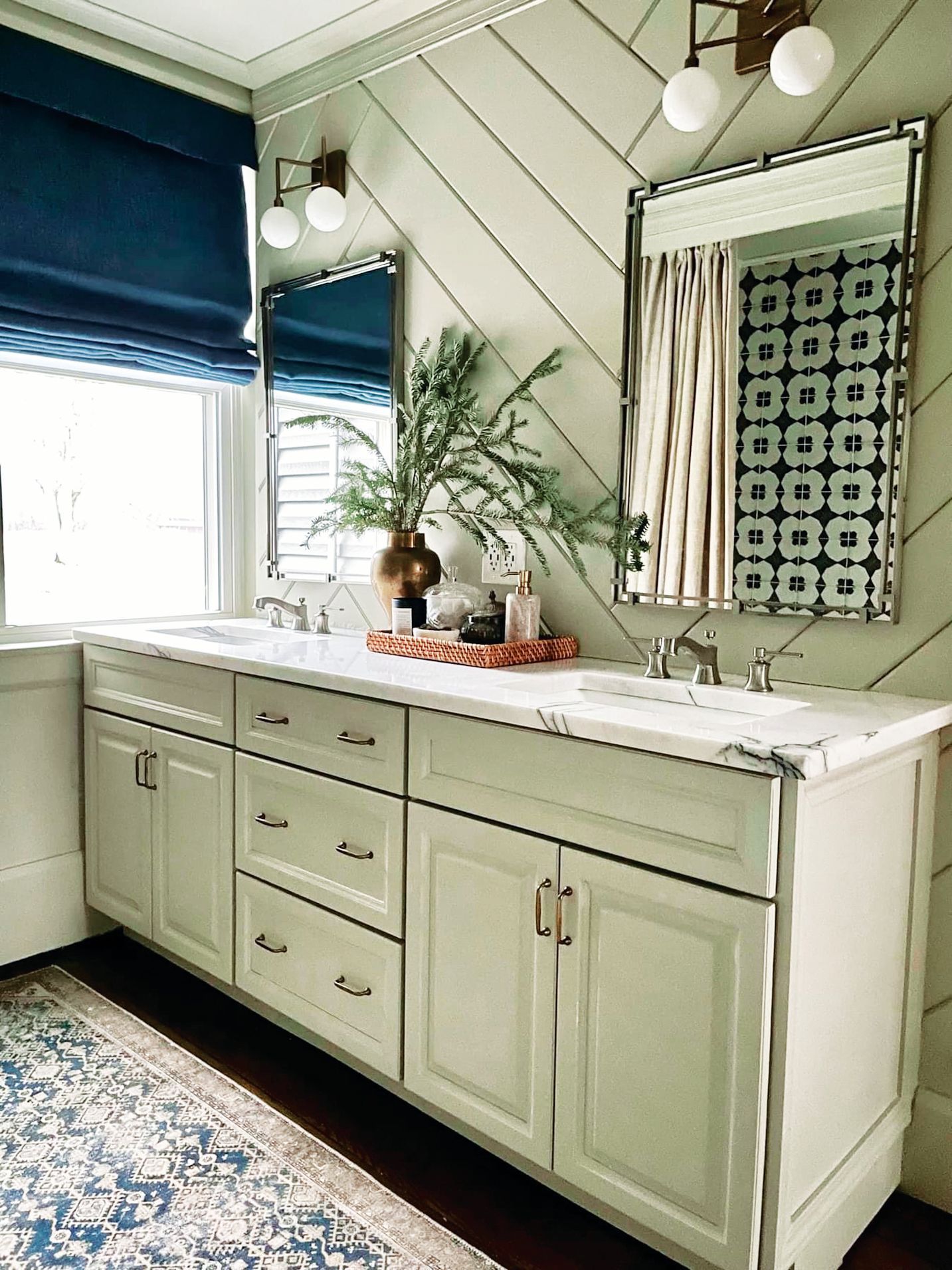 Double vanity in a bathroom with sage green diagonal shiplap walls, white marble countertop, mirrors, and blue blinds.