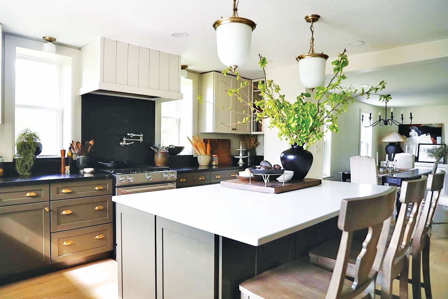 A modern kitchen with dark green cabinets, white countertops, a large center island, and two pendant lights overhead.