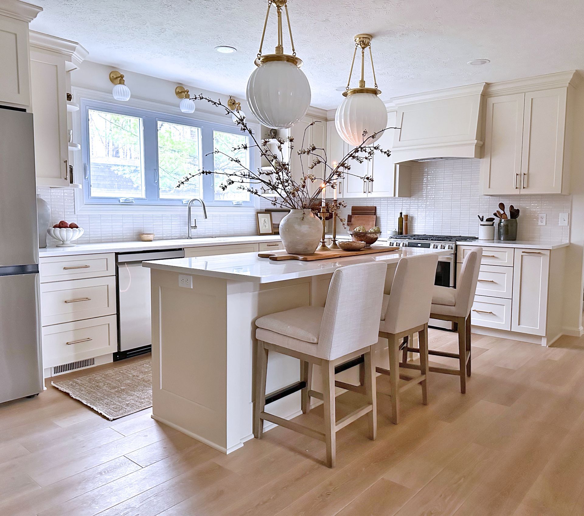 Bright, modern kitchen with white cabinets, a central island, light wood floors, and two globe pendant lights.