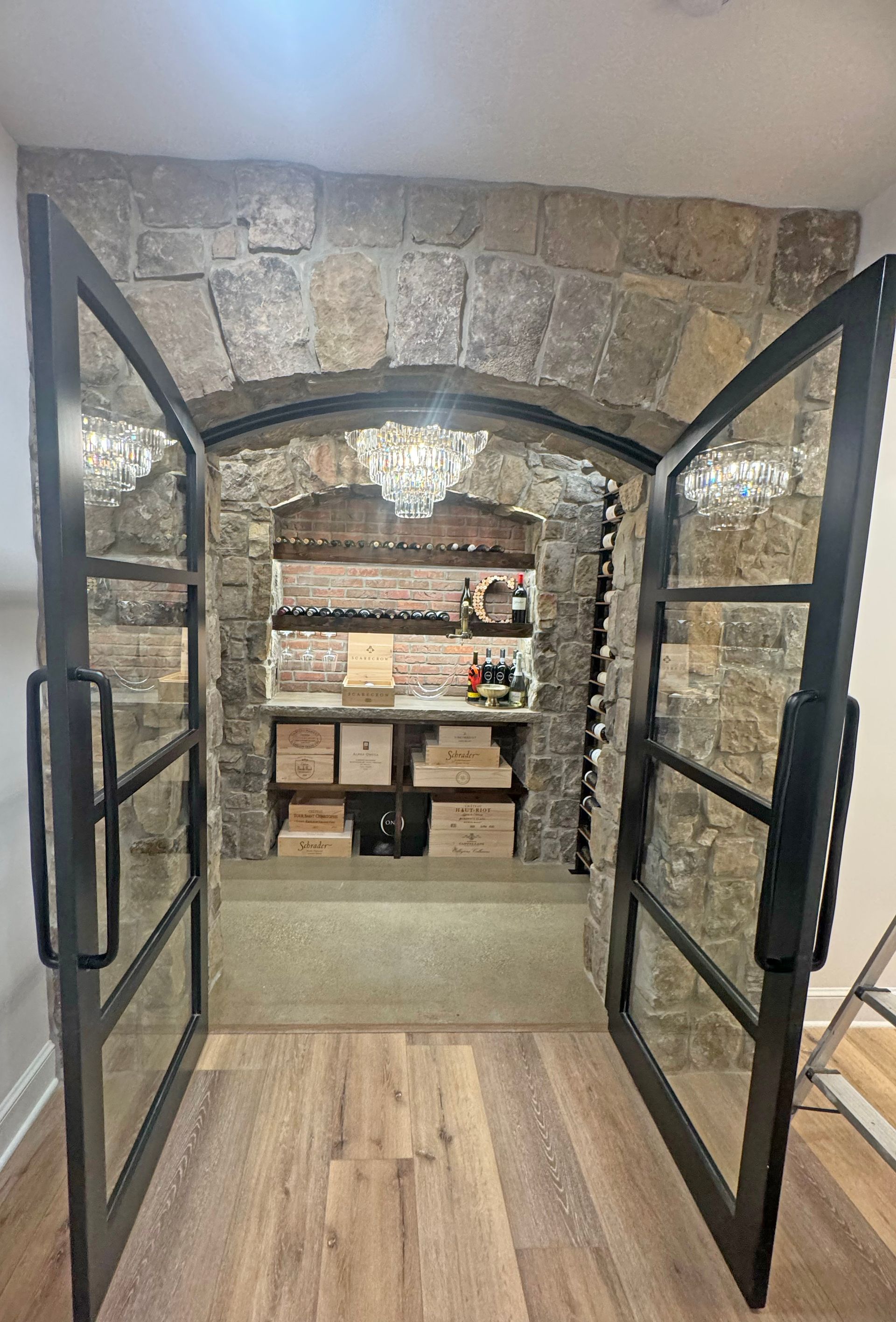 A wine cellar entrance with glass-paneled iron doors set into a stone archway, revealing wooden shelves and storage bins.