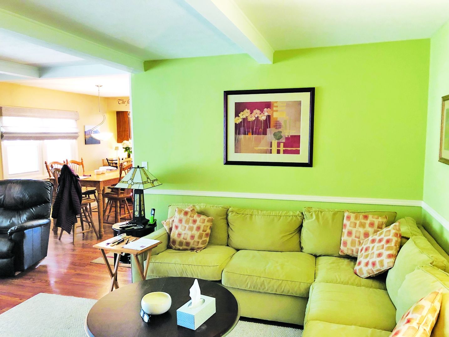 A cozy living room with a lime green sofa and walls, a dark round coffee table, and a framed art piece in the background.