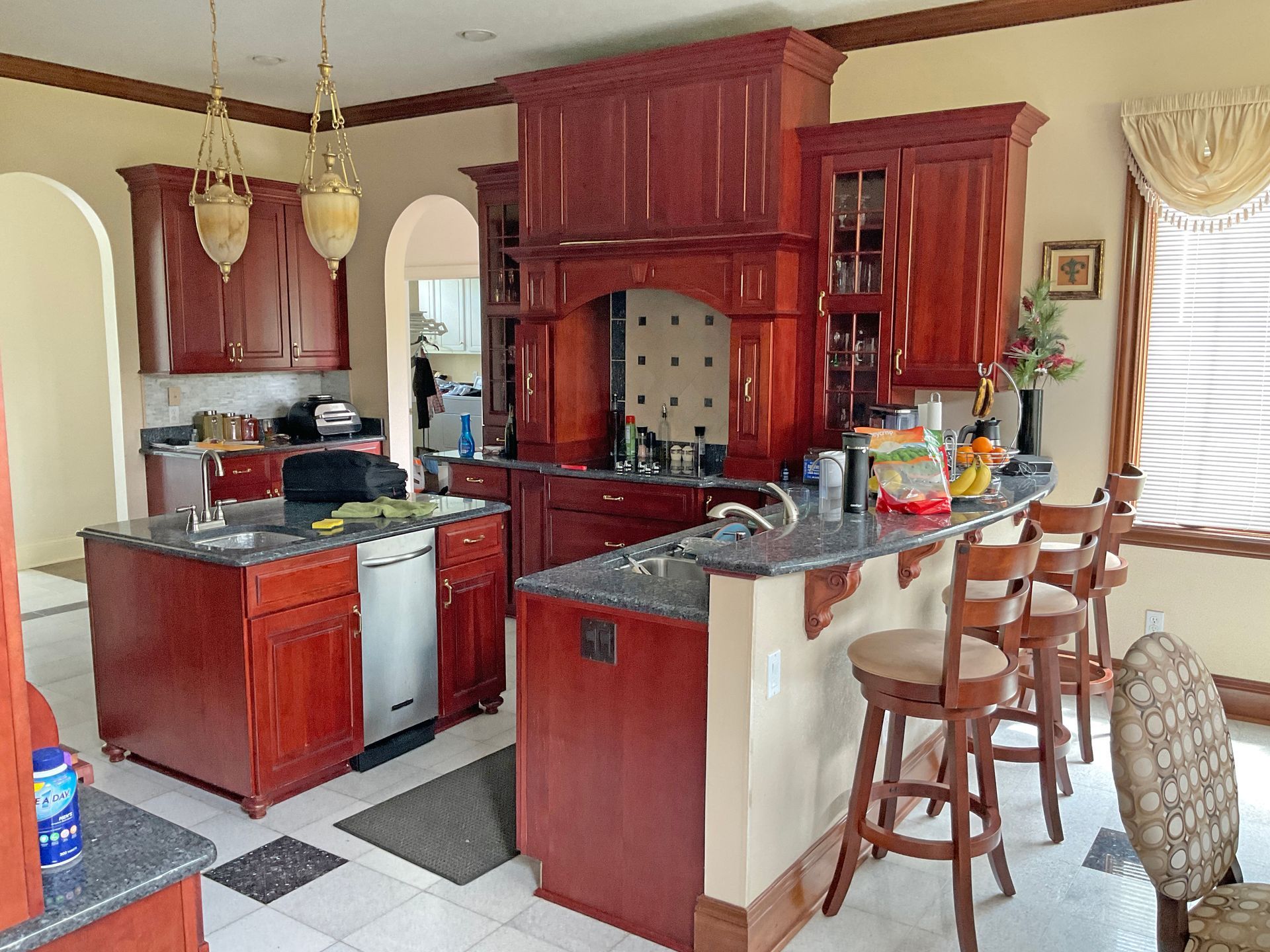 A kitchen with dark cherry-wood cabinets, a large central island, granite countertops, and two wooden bar stools.