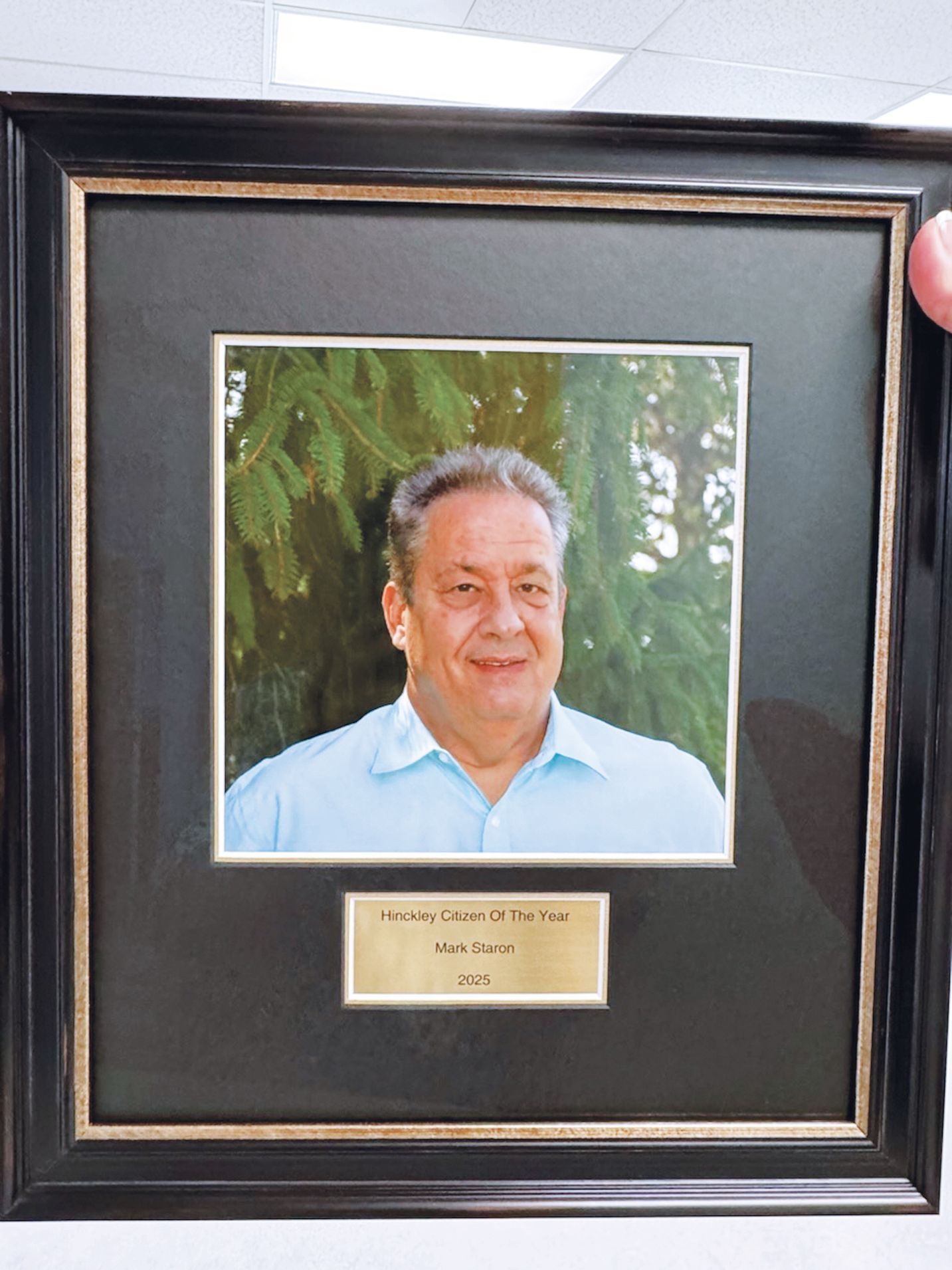 A framed portrait of a person in a light blue shirt, with a plaque below reading 