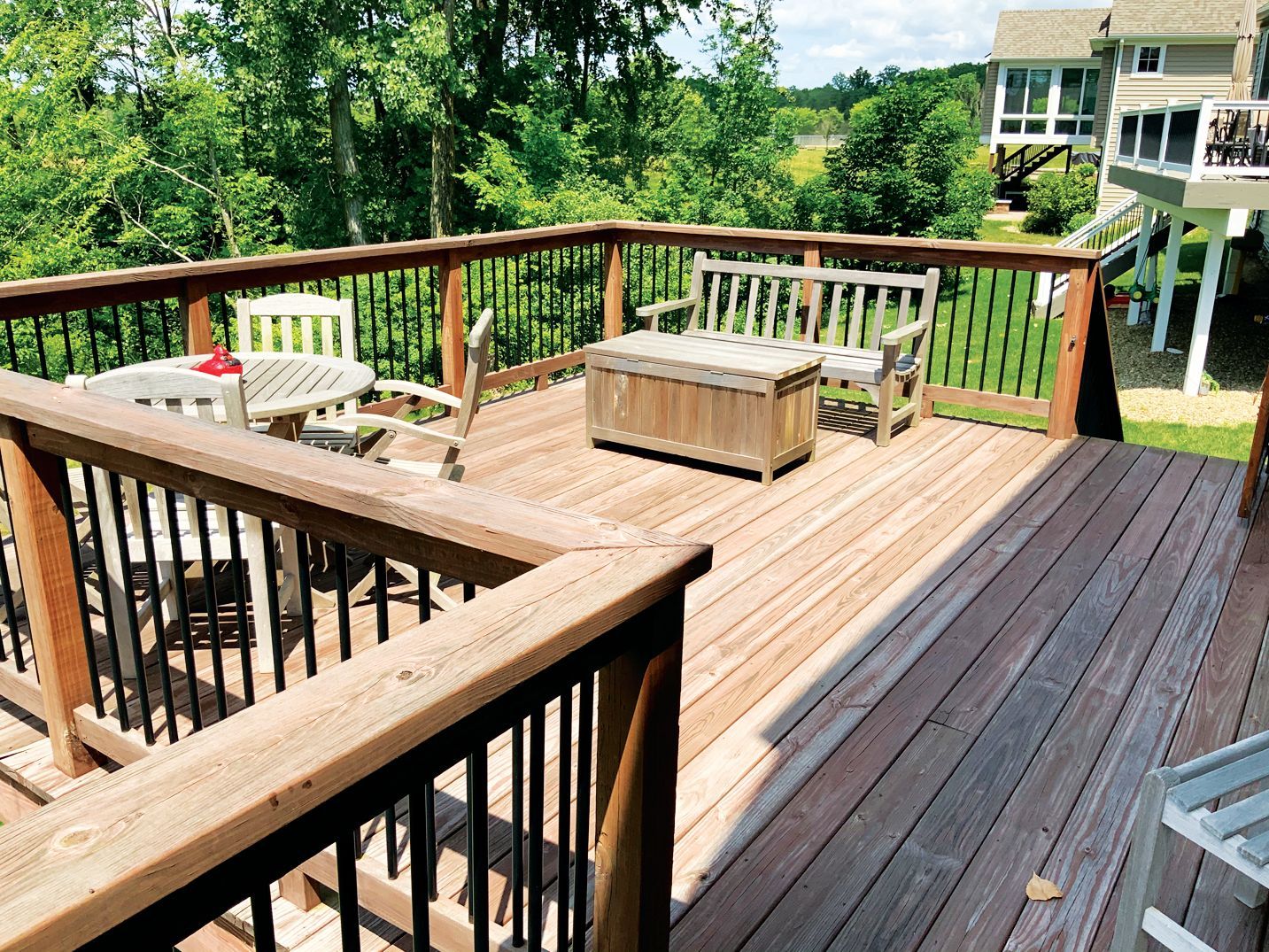 A wooden deck featuring a table with chairs and a bench, overlooking a green backyard and adjacent house.