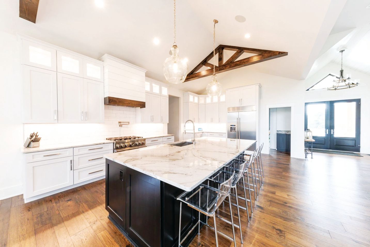 Bright kitchen with white cabinets, a dark island with marble countertop, wood floors, and exposed wooden ceiling beams.