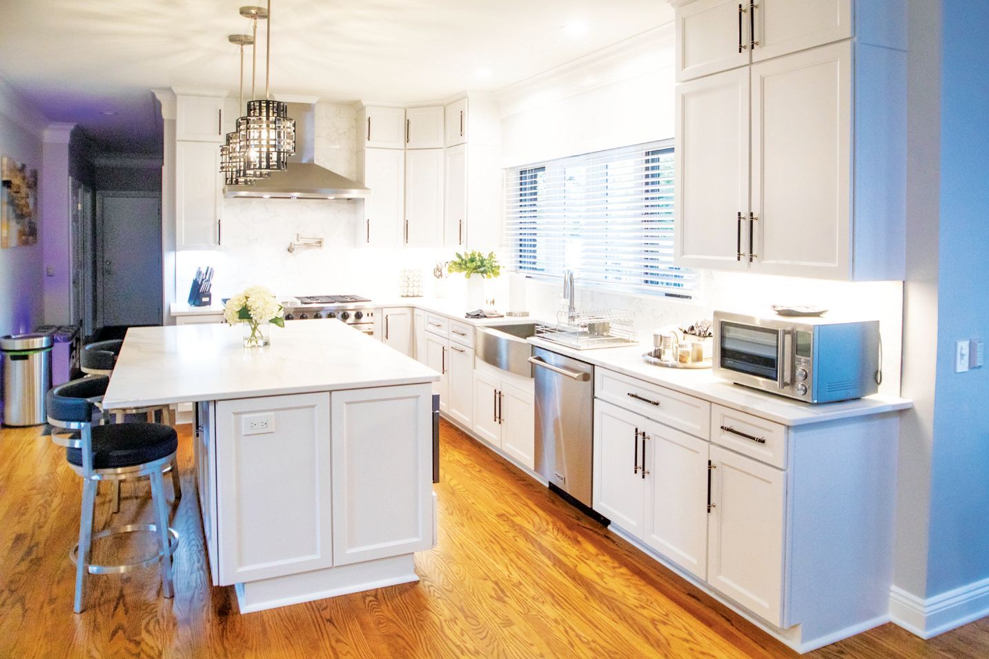 Bright, modern kitchen with white cabinetry, wooden floors, a central island, and stainless steel appliances.