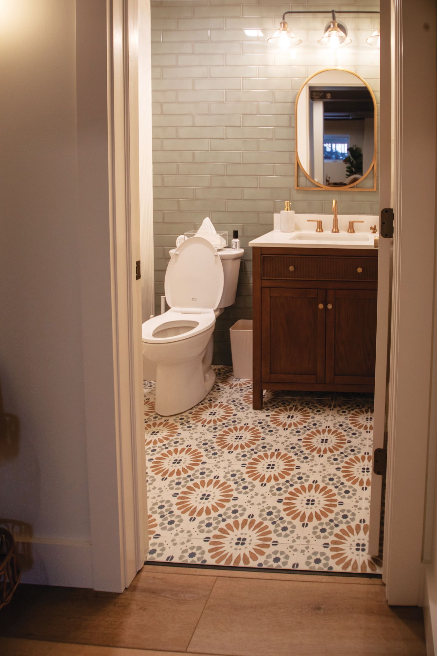 Small bathroom with a patterned tile floor, dark wood vanity, white toilet, and sage green subway tile wall.