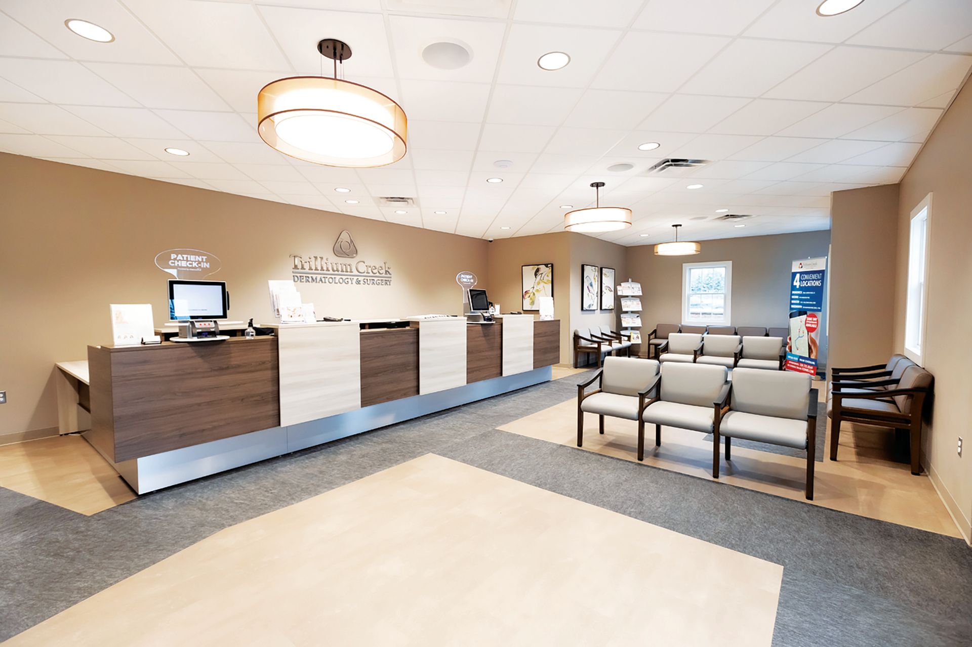 A modern medical reception area with a long desk, rows of gray chairs for patients, and neutral-toned walls.