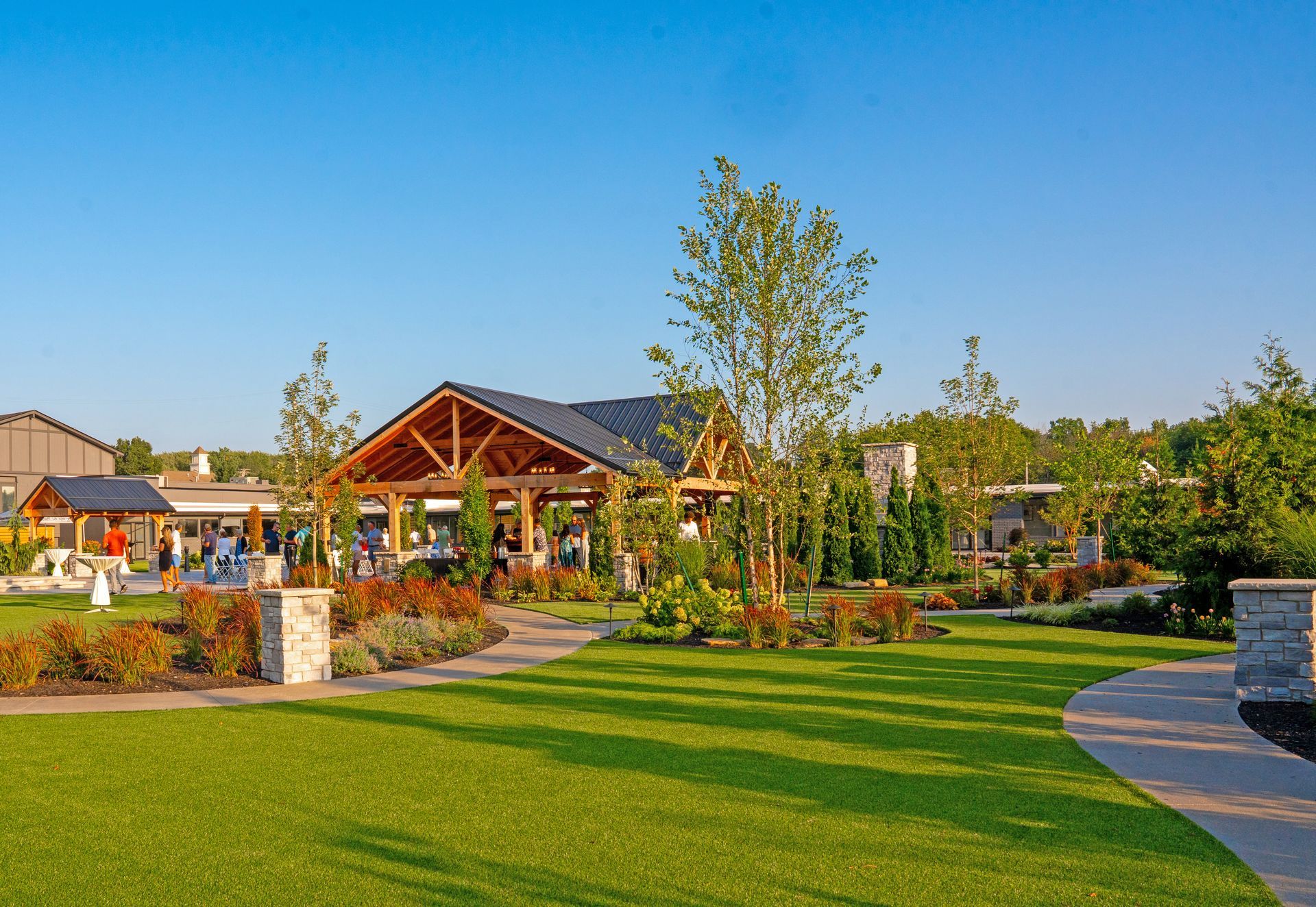 A well-manicured lawn with a stone path leading to a timber-frame pavilion under a clear blue sky.