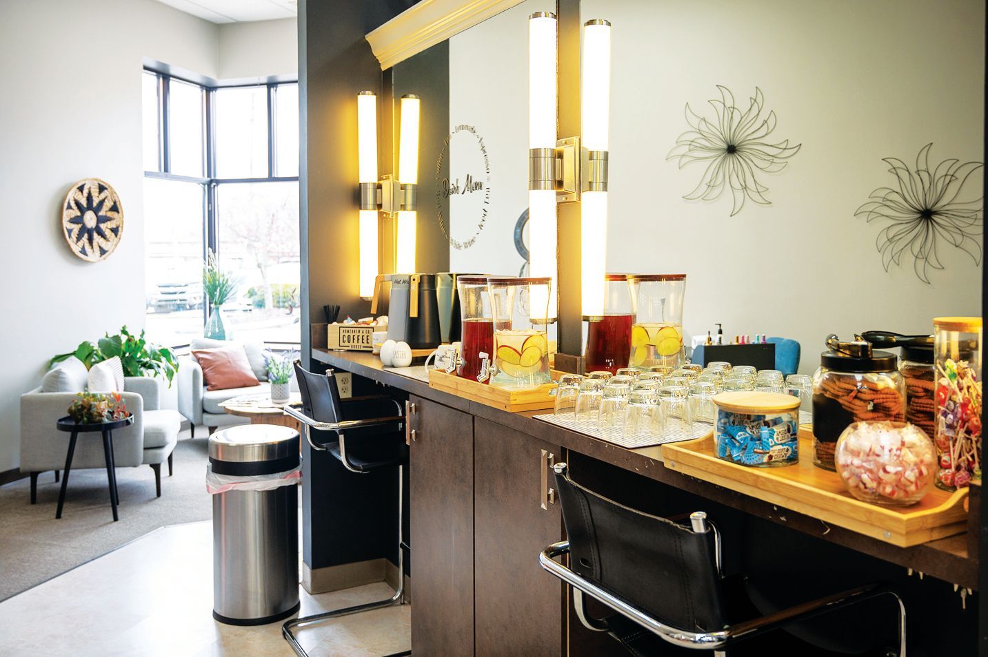 A waiting area with a drink station, bar stools, and a seating area with a sofa and windows.
