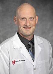 A professional headshot of a smiling medical provider in a white lab coat with a University Hospitals logo.