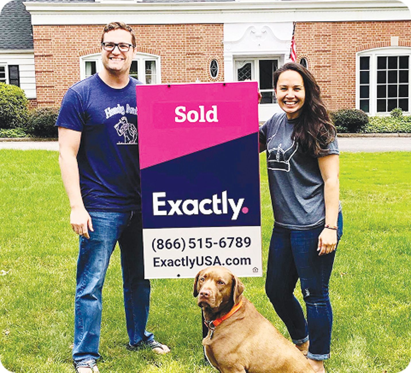 A couple and their dog stand on a lawn in front of a house, holding a 