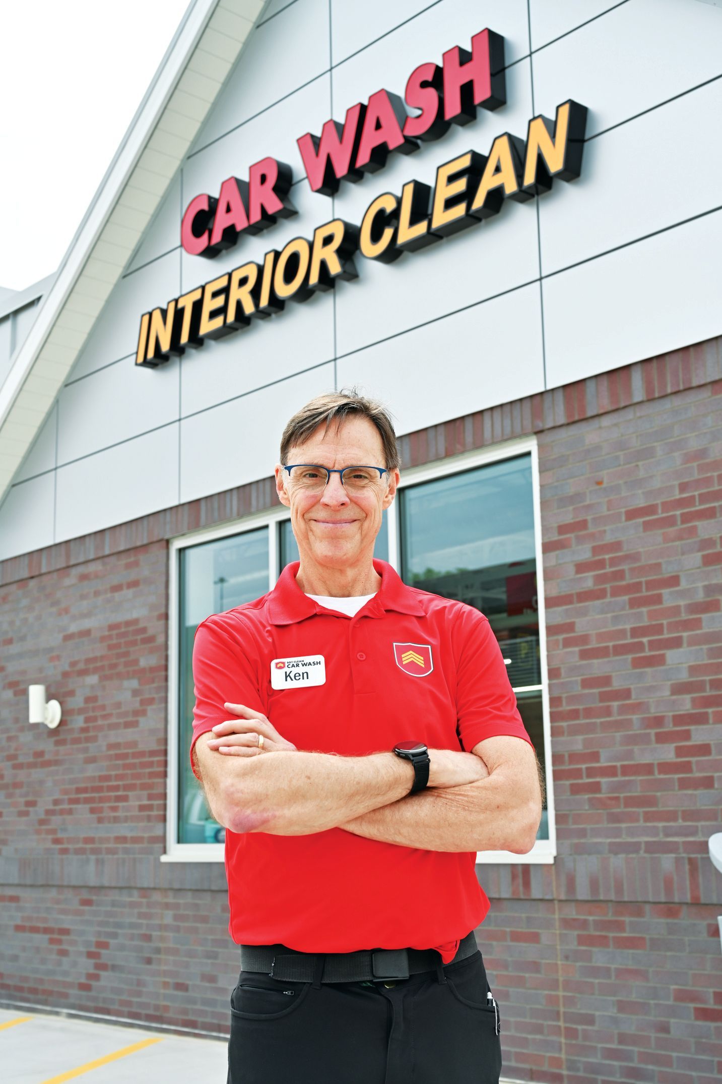 A person in a red uniform stands with arms crossed in front of a building labeled 