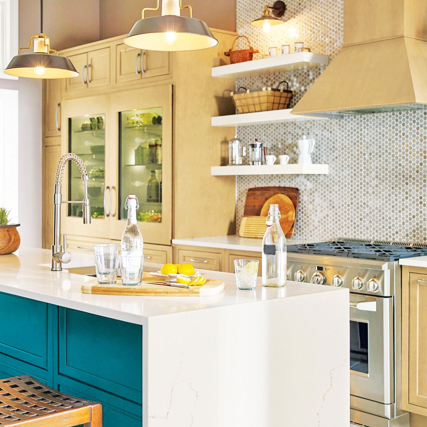 A modern kitchen featuring a teal island with white countertops, light wood cabinetry, white shelves, and pendant lighting.