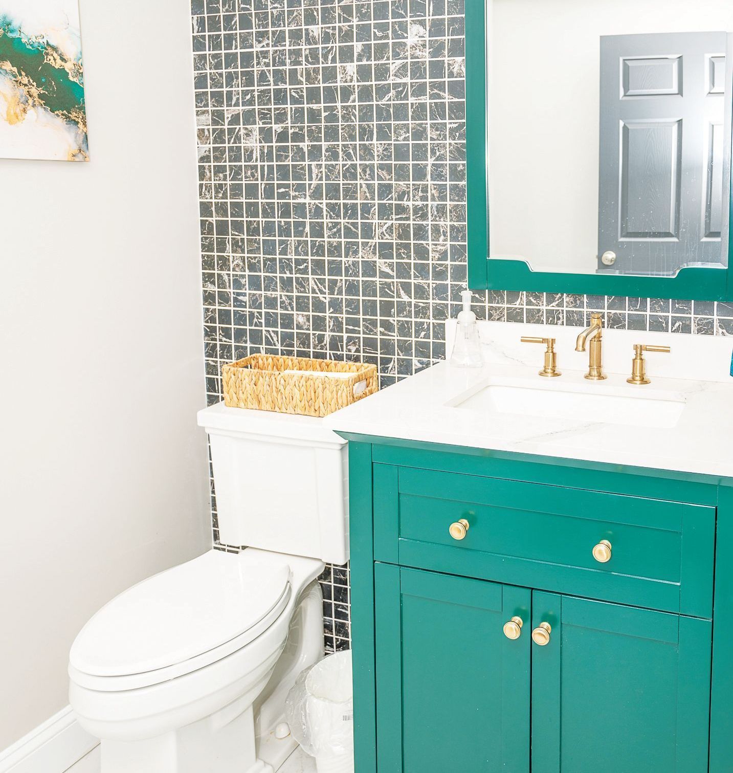A small bathroom featuring a teal vanity with gold hardware, a white sink, and a gray square-tiled accent wall.