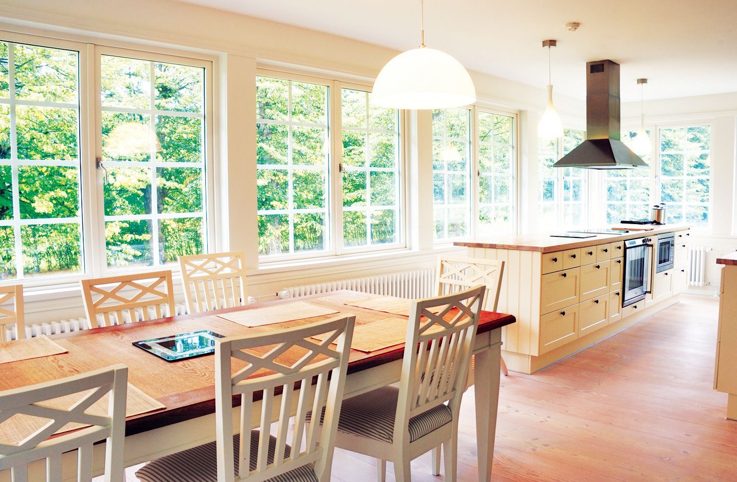 A bright kitchen with a wooden dining table and white chairs next to large windows, leading to an island with a stove.