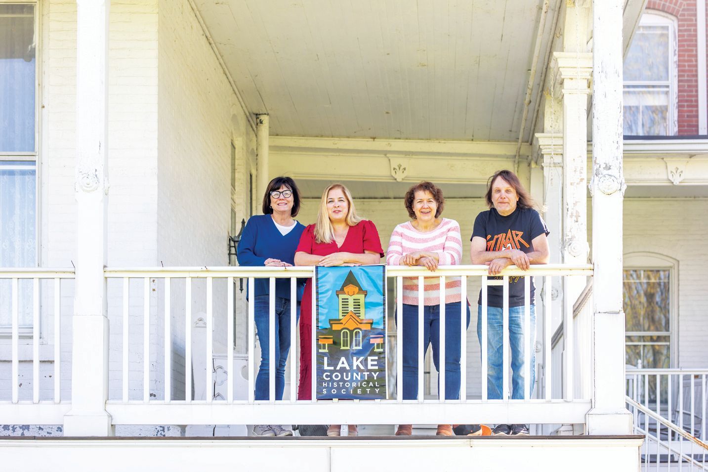 Four people stand on a porch behind a sign reading 