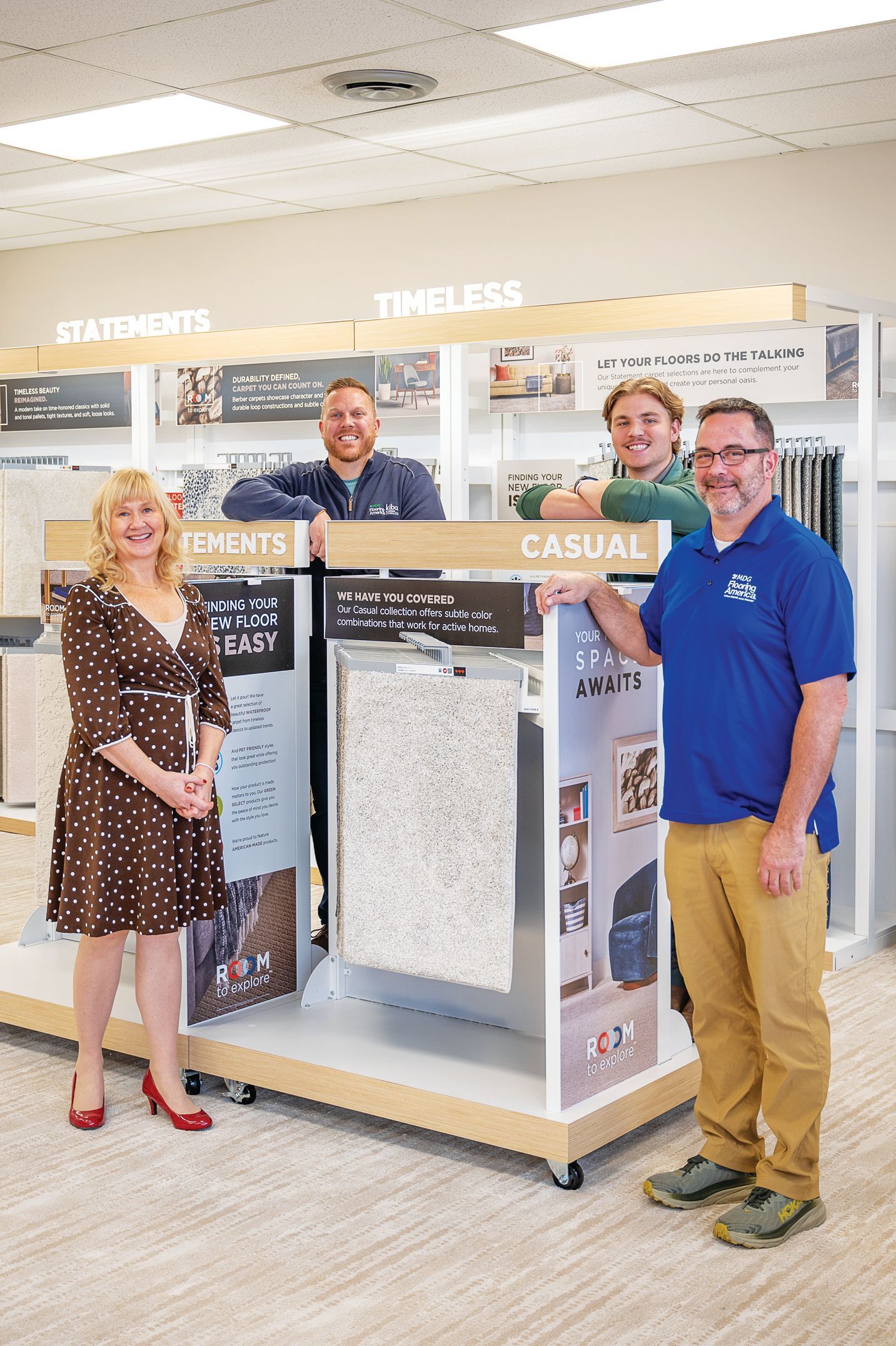 Four people pose in a store display area showcasing flooring products, with signs labeled 