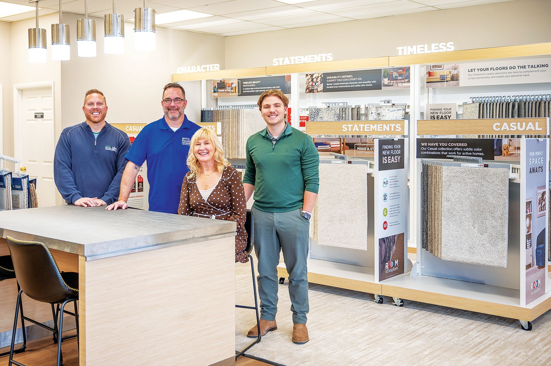Four people stand together behind a counter in a home design or flooring retail showroom featuring sample displays.