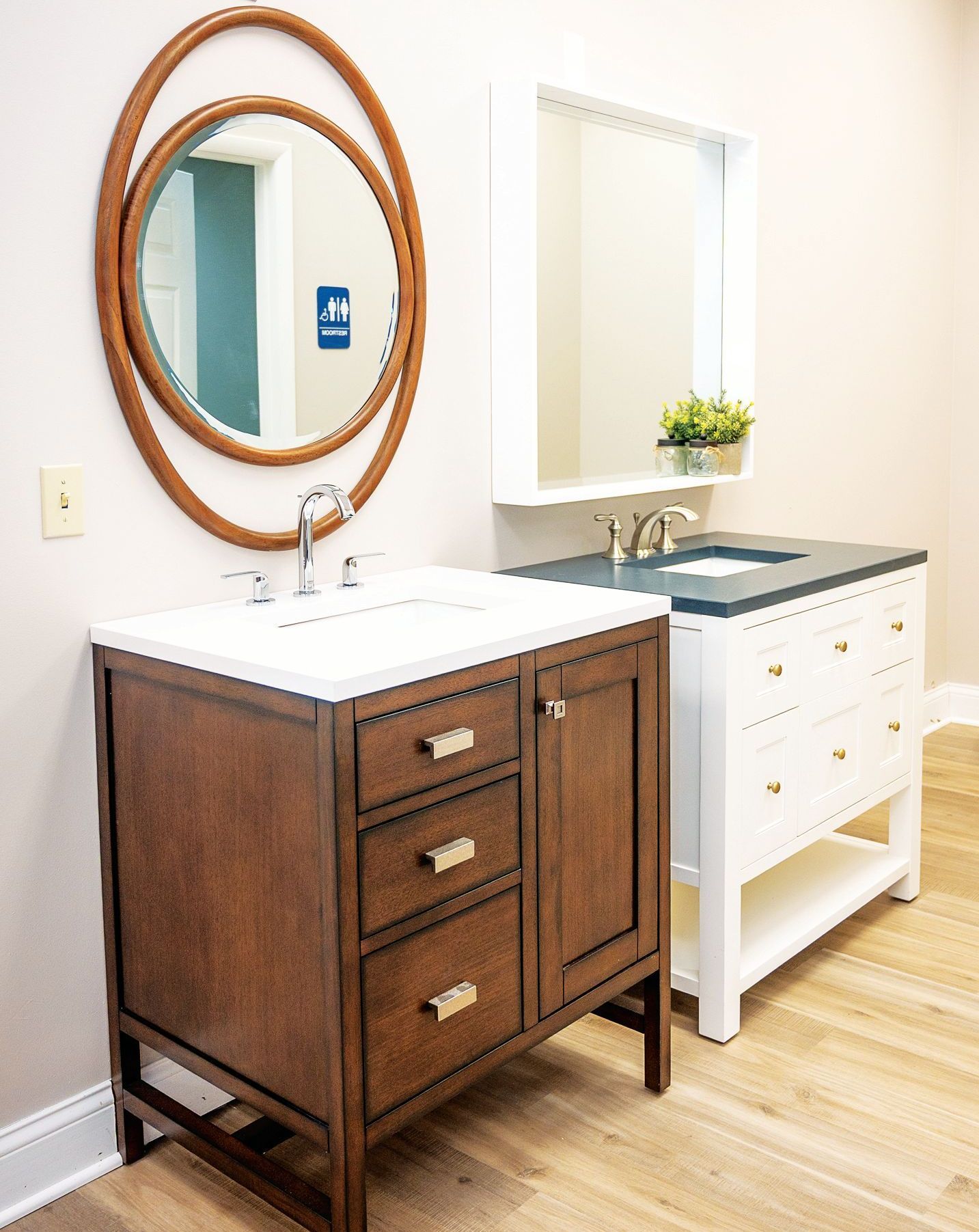 A bathroom vanity setup featuring a wood cabinet with a round mirror next to a white vanity with a rectangular mirror.