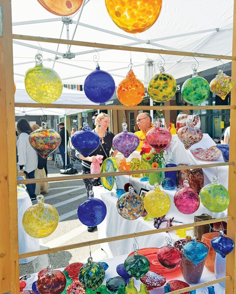 A display of colorful, hand-blown glass ornaments hanging from a wooden rack at an outdoor market.
