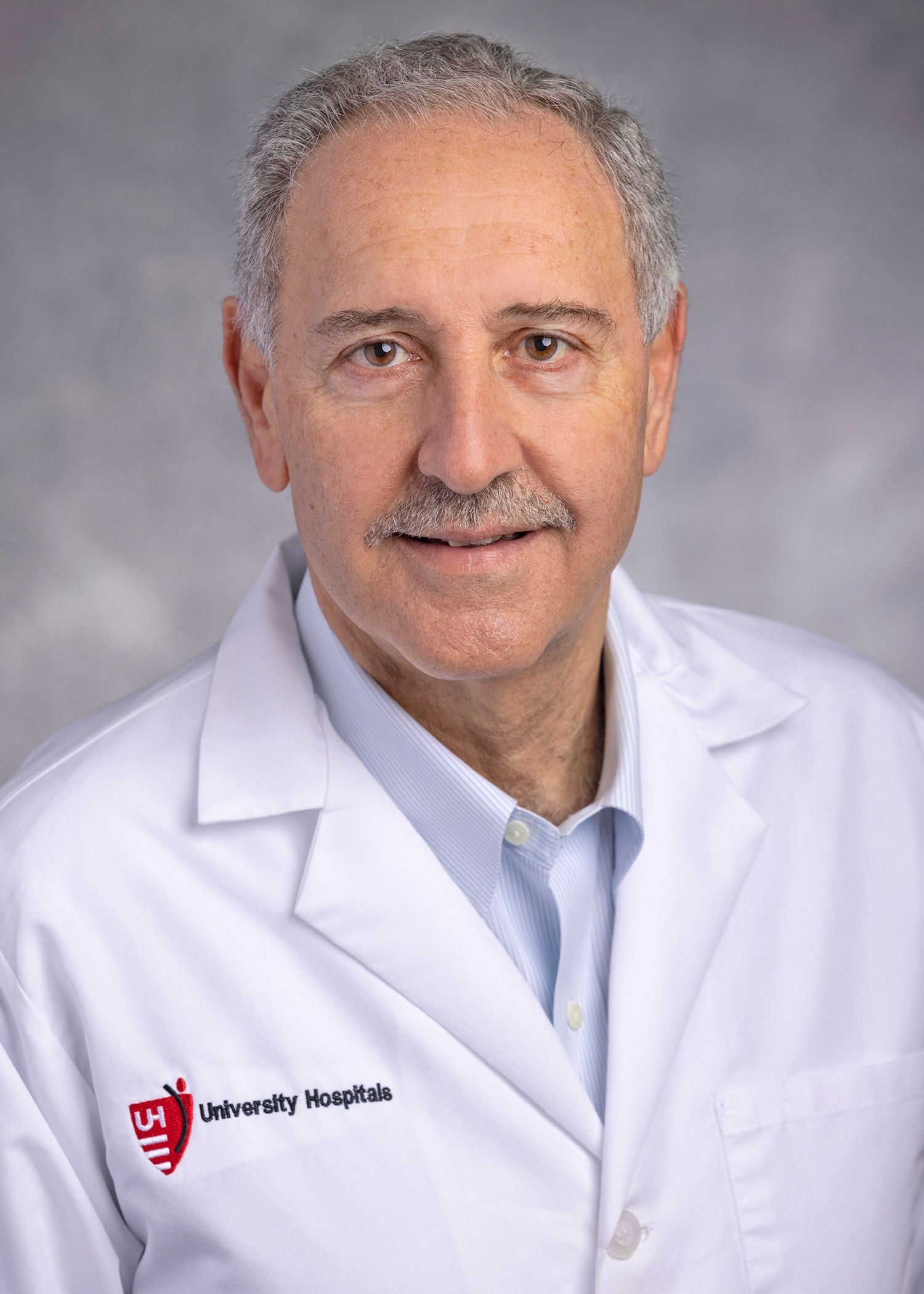 Headshot of a doctor in a white coat with the University Hospitals logo against a light grey background.
