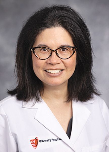 Headshot of a smiling medical professional wearing a white coat with a University Hospitals logo, against a grey backdrop.