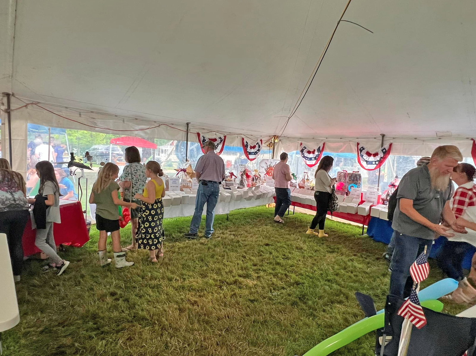 People browsing stalls inside a large white tent decorated with patriotic bunting.