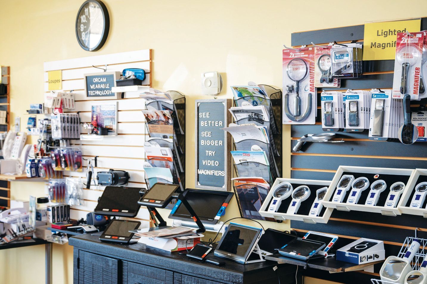 A retail display of electronic gadgets, including magnifying devices, tablet stands, and accessories on wall-mounted racks.