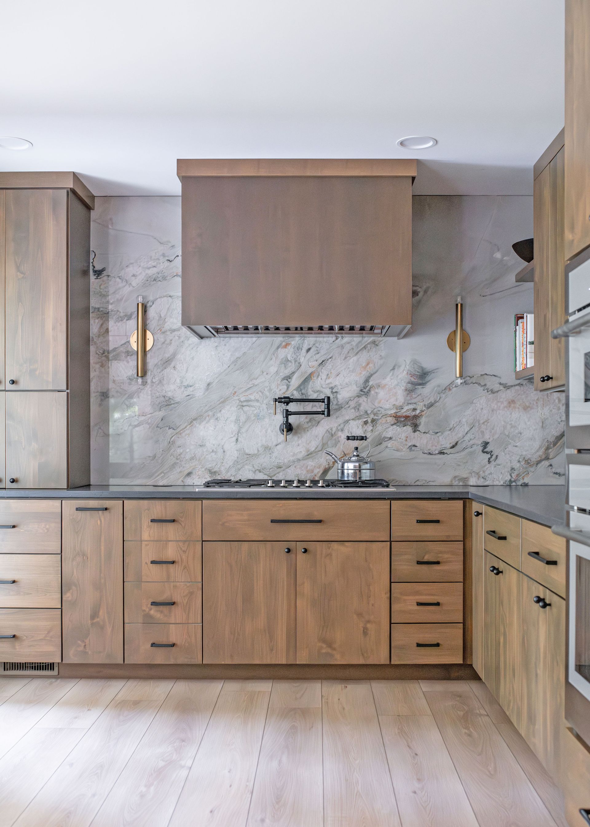 Modern kitchen with natural wood cabinets, a large marble backsplash, and a wooden vent hood above the stovetop.