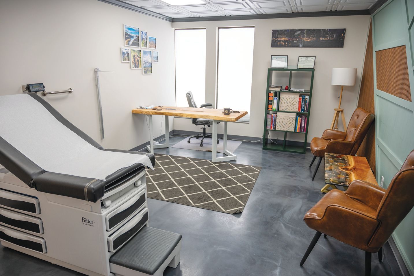 Medical office with an exam table, desk, chairs, and shelving against a teal wall and neutral-colored walls.