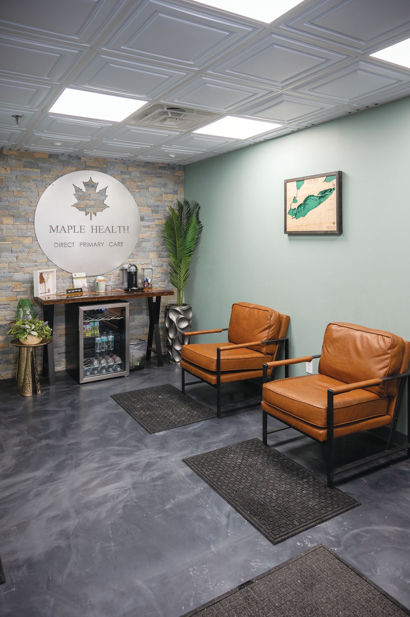 A reception area with two tan leather chairs, a stone accent wall featuring a logo, a small fridge, and a framed map.