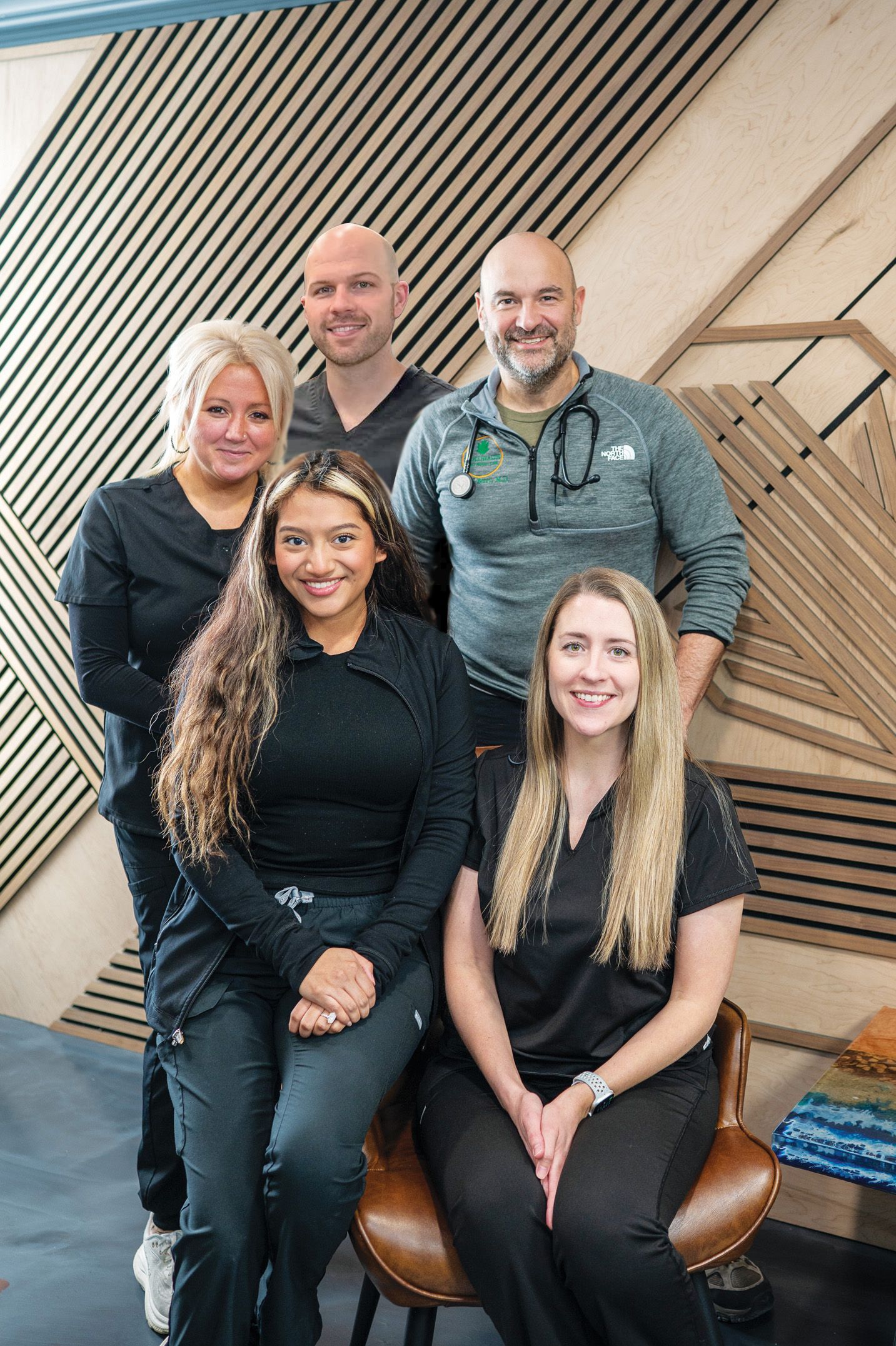 A group of five professionals in medical scrubs poses for a portrait against a modern slatted wood background.