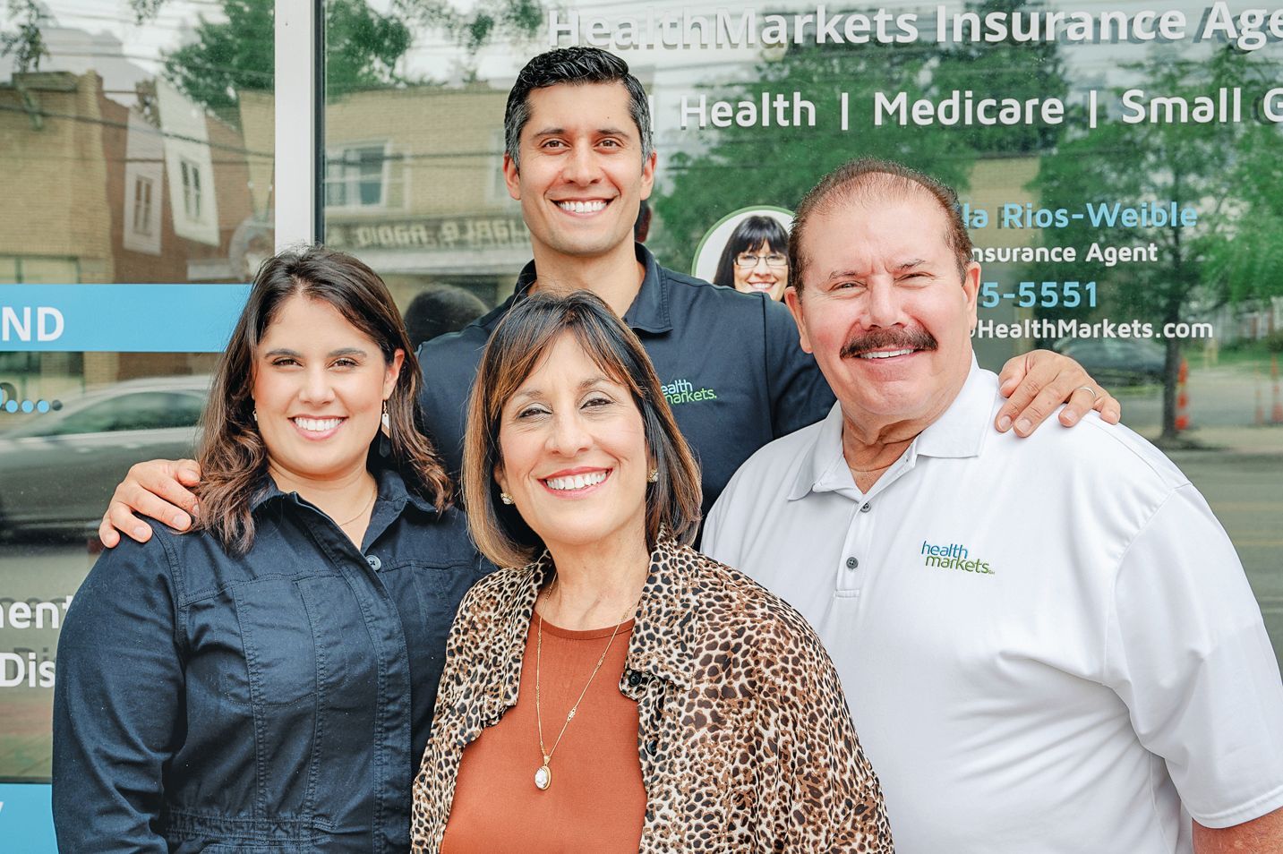 Four people stand outside a HealthMarkets insurance office, smiling at the camera.