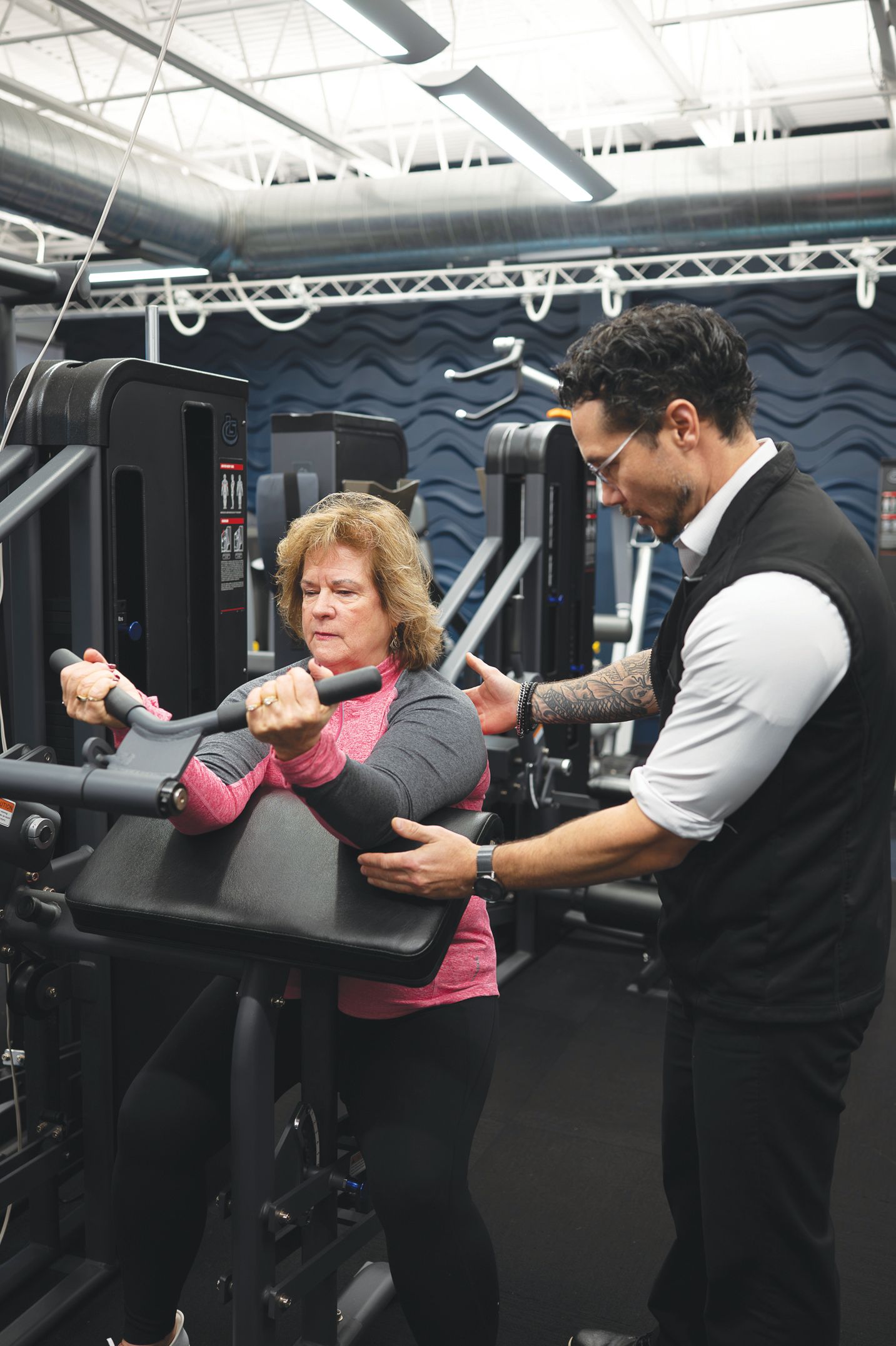 A fitness professional guides a person performing a bicep curl exercise on a gym machine.