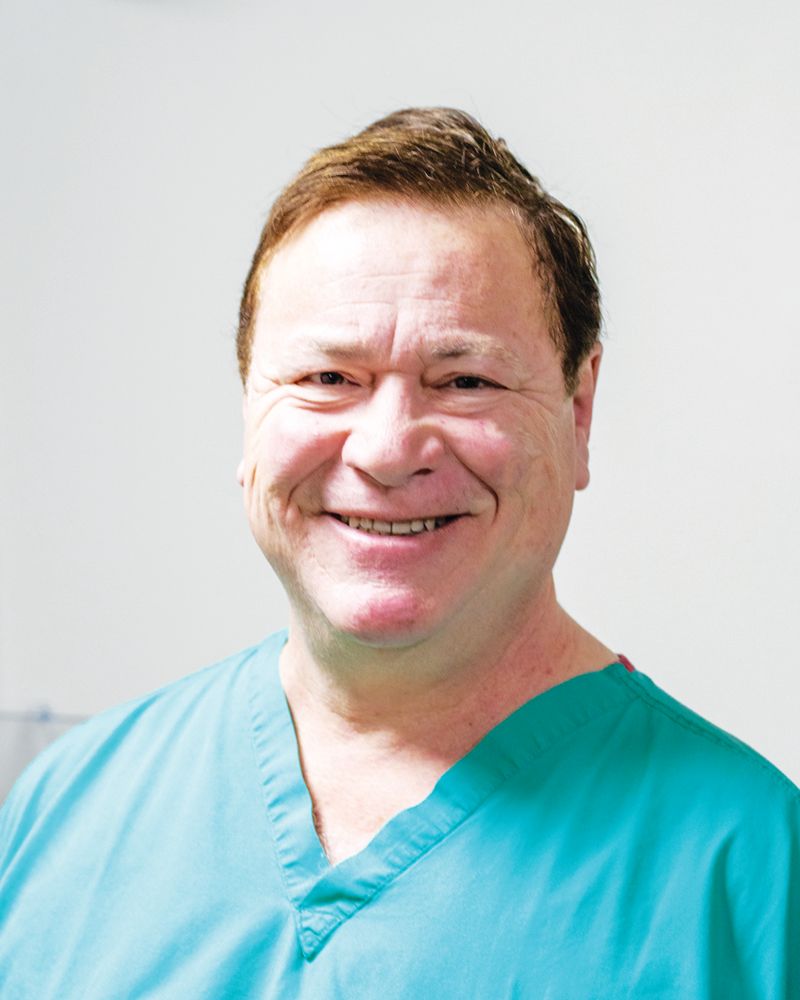 A person wearing teal medical scrubs smiles while looking directly at the camera against a white background.