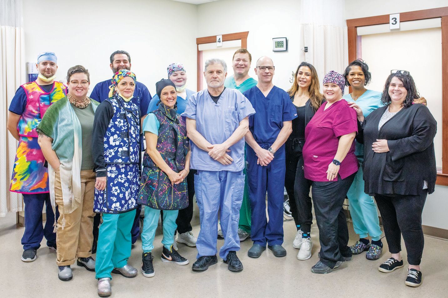 A group of healthcare professionals in scrubs and casual attire stand together smiling in a clinical hallway.