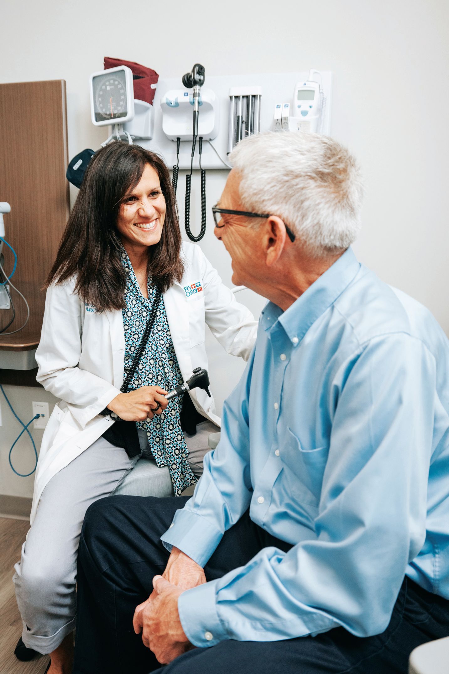 A medical provider in a white coat smiles while speaking with a patient in an exam room.