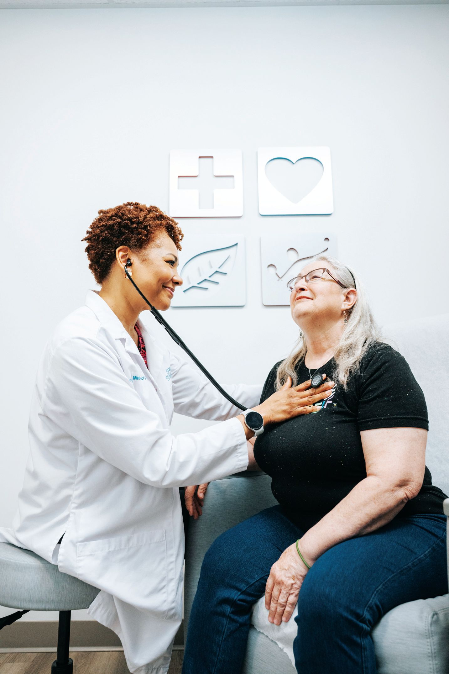 A medical professional listens to a patient's heartbeat with a stethoscope in a clinic with wall art.