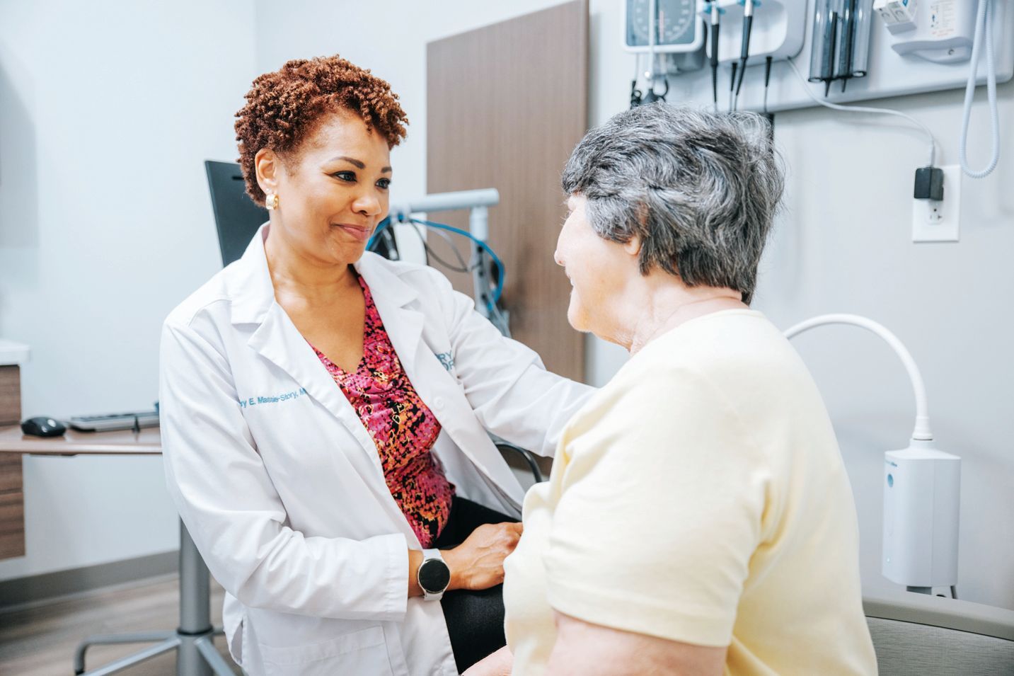 A healthcare professional in a lab coat sits with a patient in a medical office, providing attentive and supportive care.