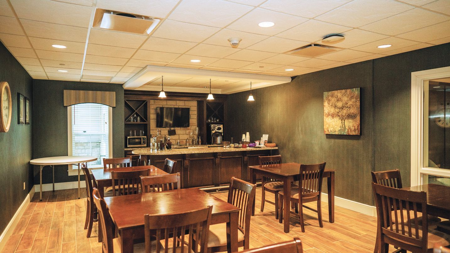 A breakfast room with dark green walls, wooden tables and chairs, and a buffet station with a coffee machine and snacks.