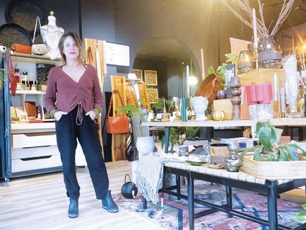 A person stands in a shop filled with home decor, including vases, plants, and shelving units, with a rug on the floor.