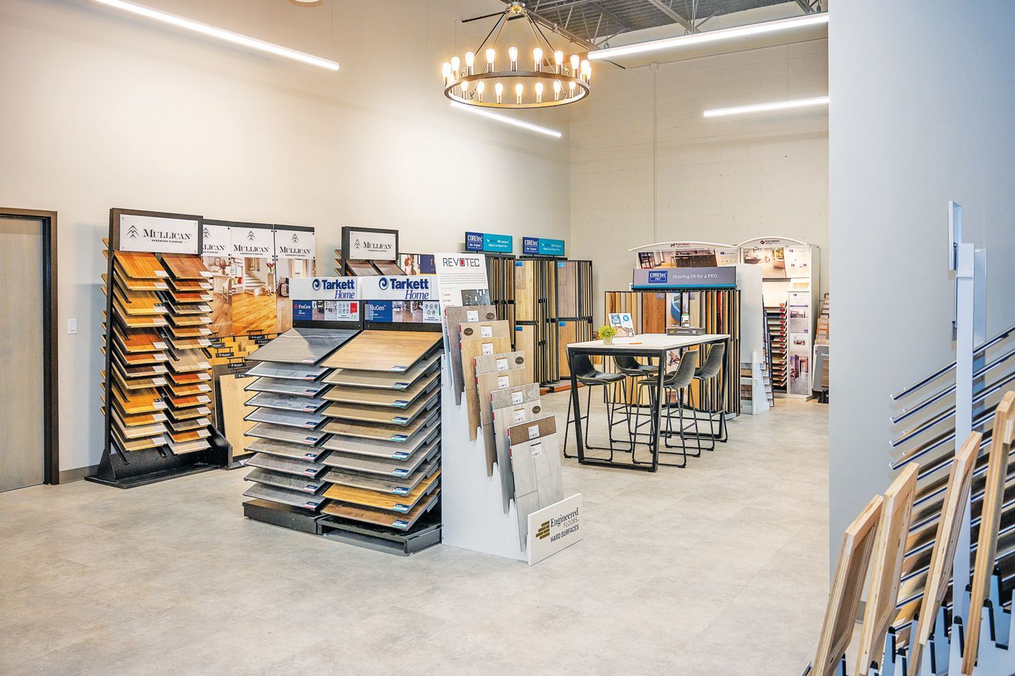A showroom featuring displays of various flooring samples, including wood planks and tiles, with a table and chairs.