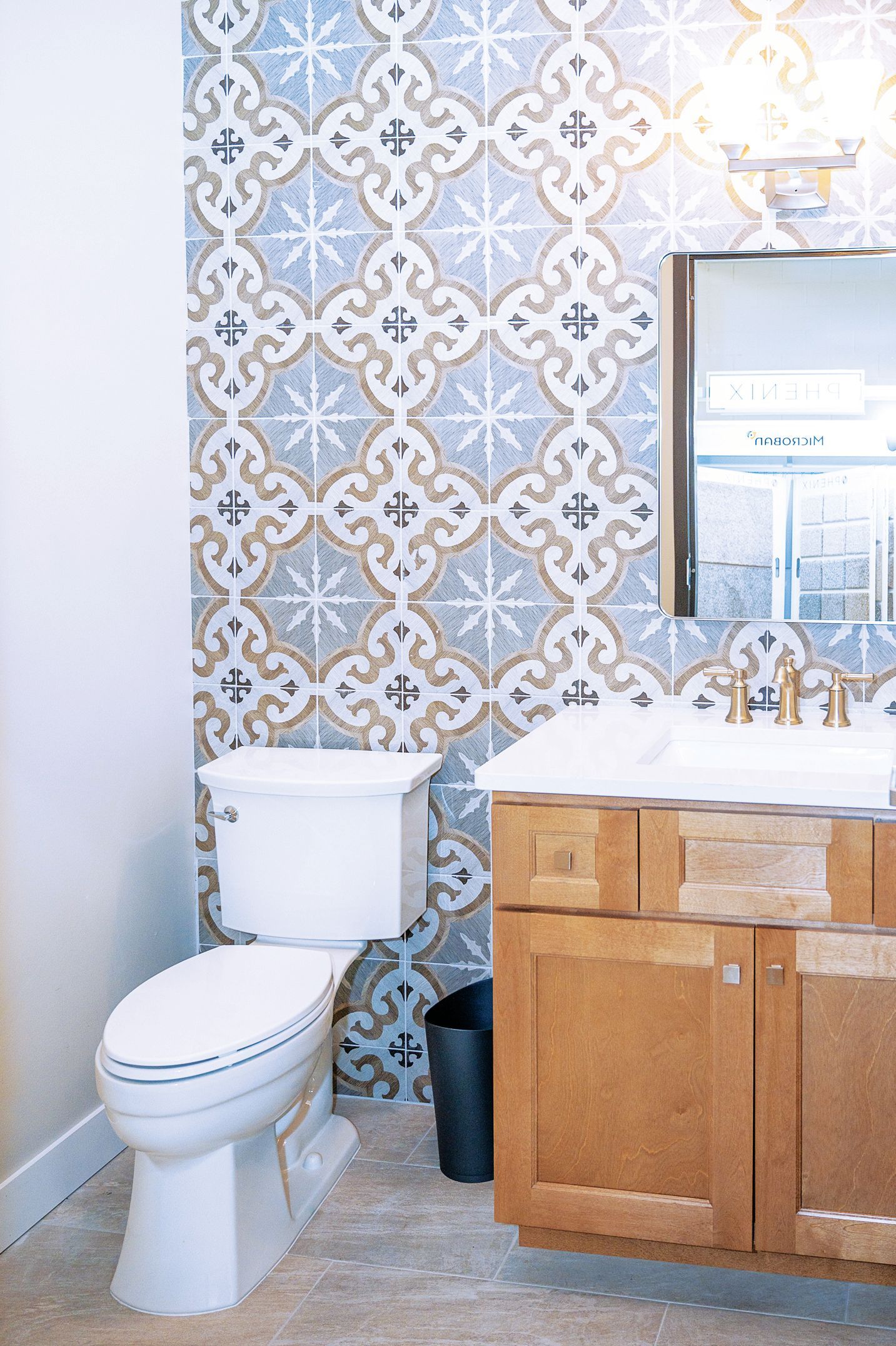 A bathroom with a patterned blue and white tile wall, a wooden vanity with a white sink, and a white toilet.