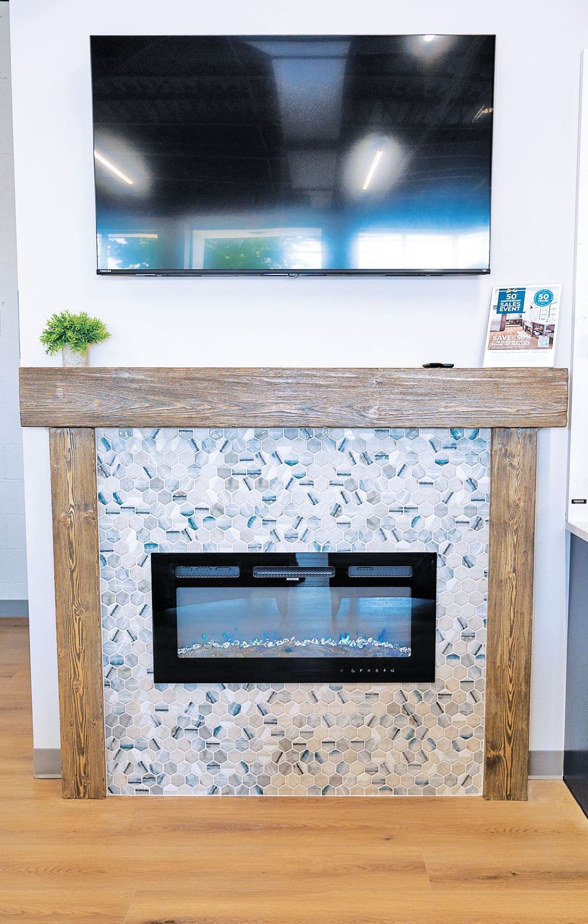 A flat-screen TV mounted above a rustic wood-framed fireplace with blue and white patterned tile and a small green plant.