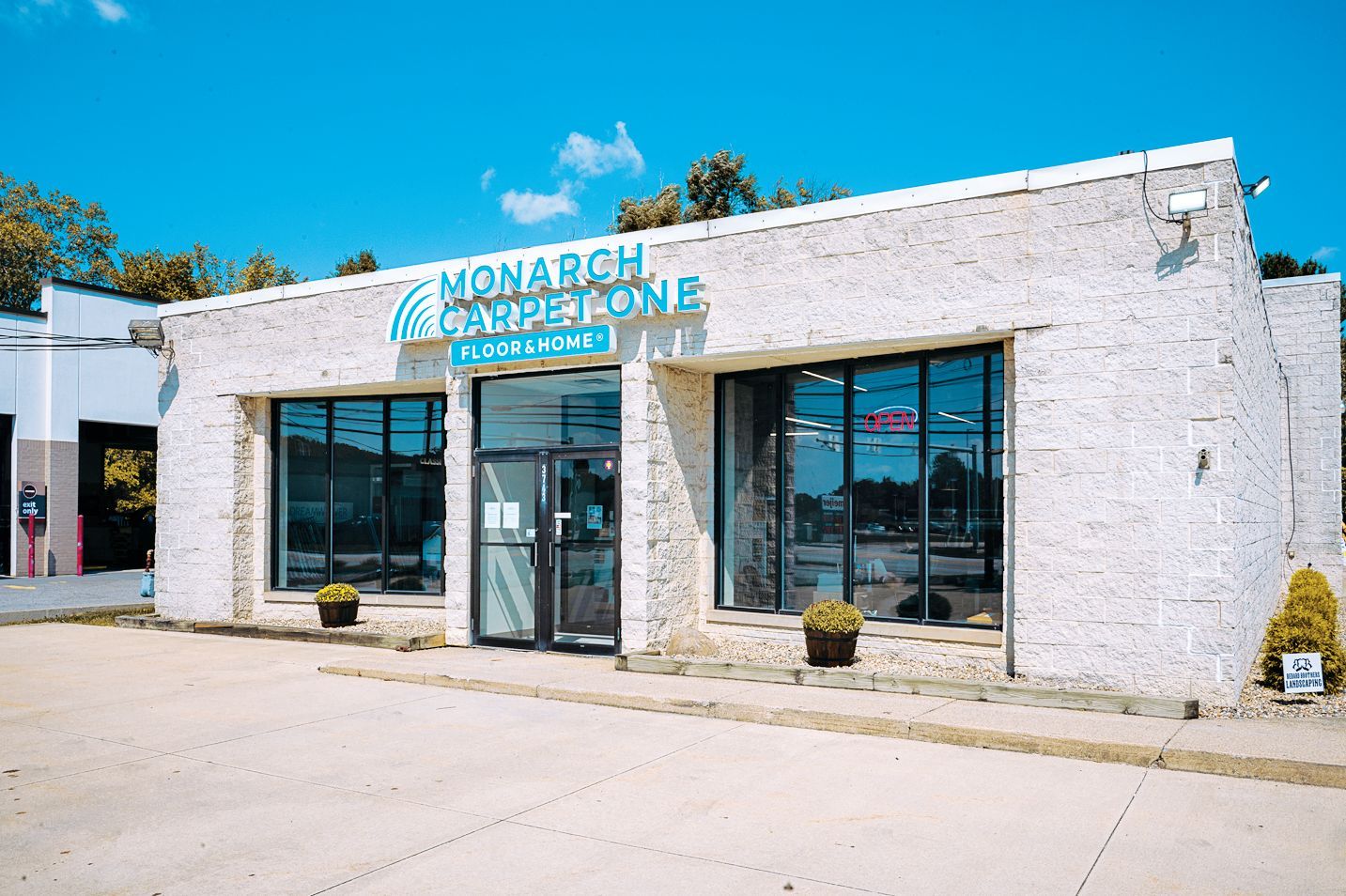 The Monarch Carpet One Floor & Home storefront features a white textured exterior with large windows and a glass door.