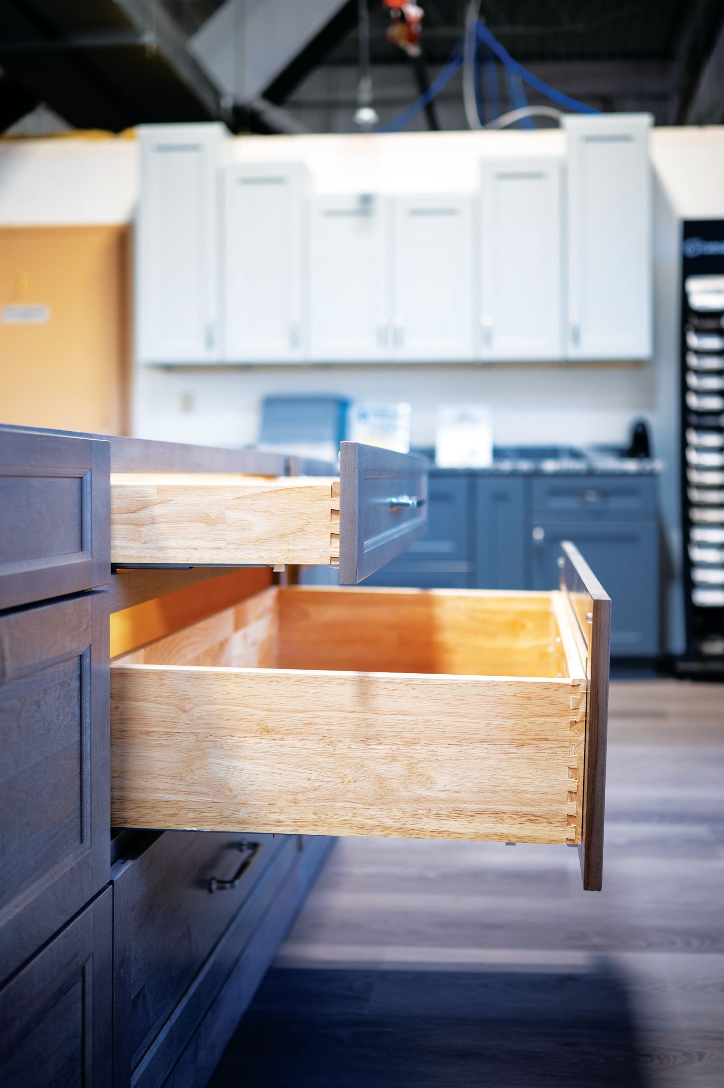 A close-up view of open kitchen drawers showing raw wood construction against a background of white and blue cabinets.