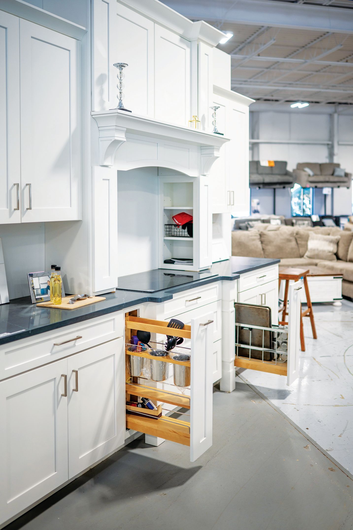 White kitchen cabinetry with open spice and kitchen utensil pull-out organizers in a showroom setting.