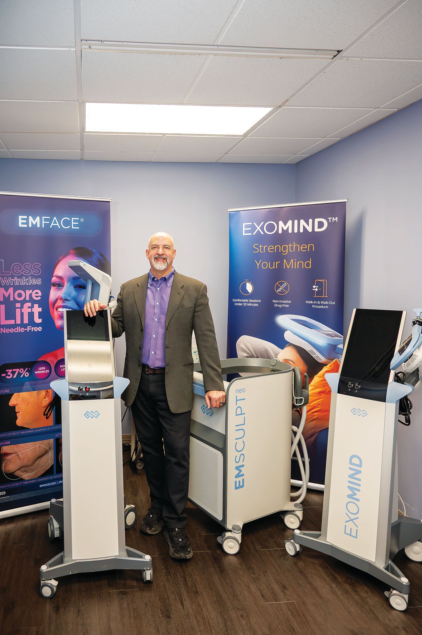 A professional standing between medical aesthetic devices with branded banners in a clinical office setting.